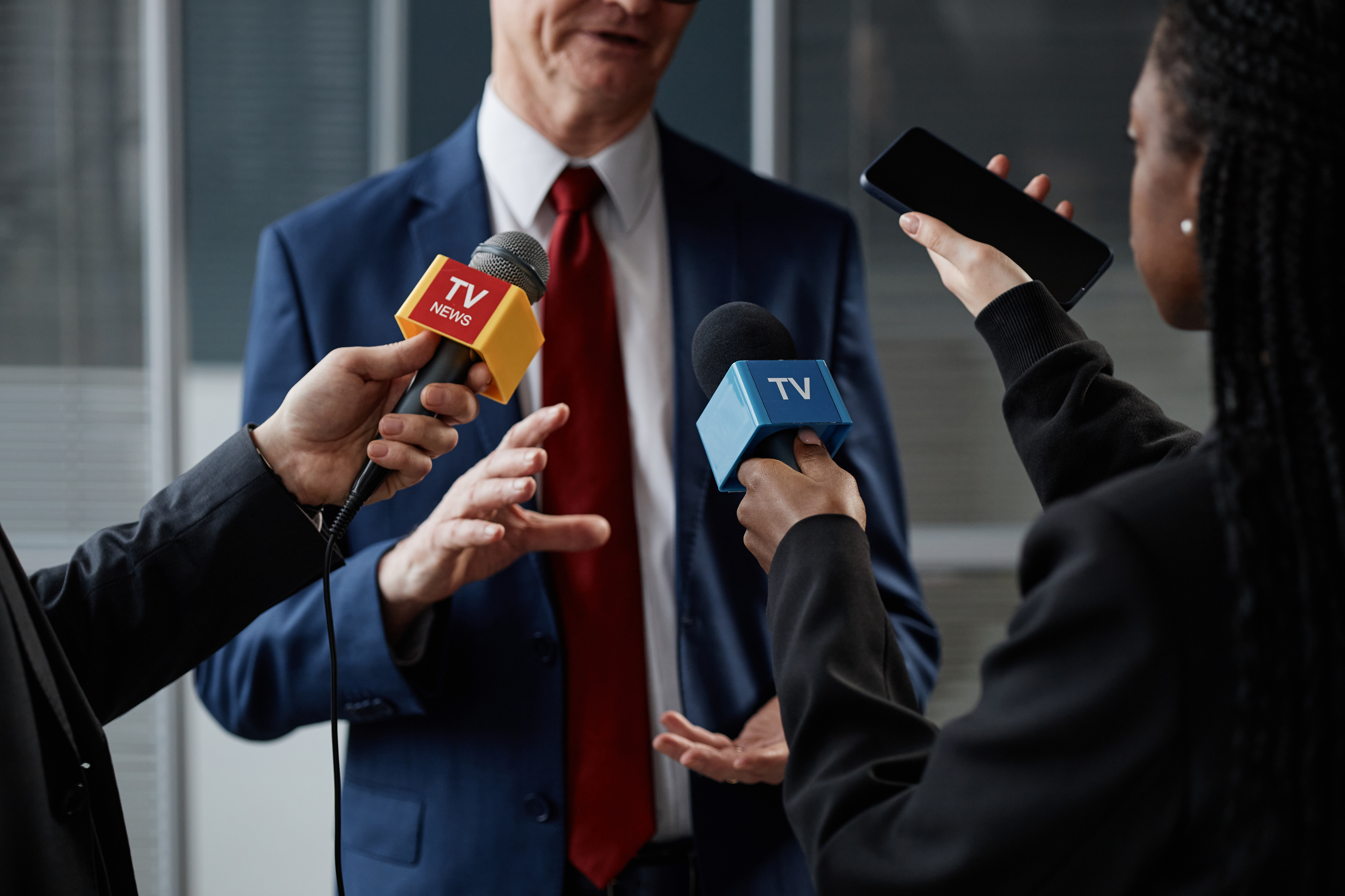 Middle Aged Caucasian Man Giving Interview to Multiethnic Journalists Indoors